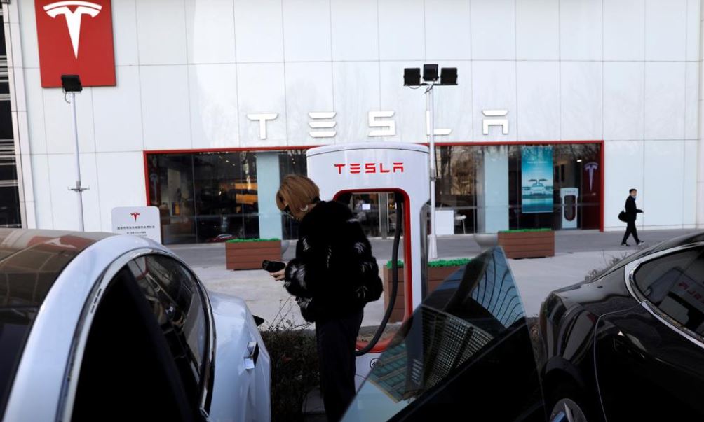 A woman charges a Tesla car in front of the electric vehicle maker's showroom in Beijing