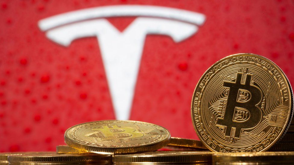 Representations of virtual currency Bitcoin are seen in front of Tesla logo