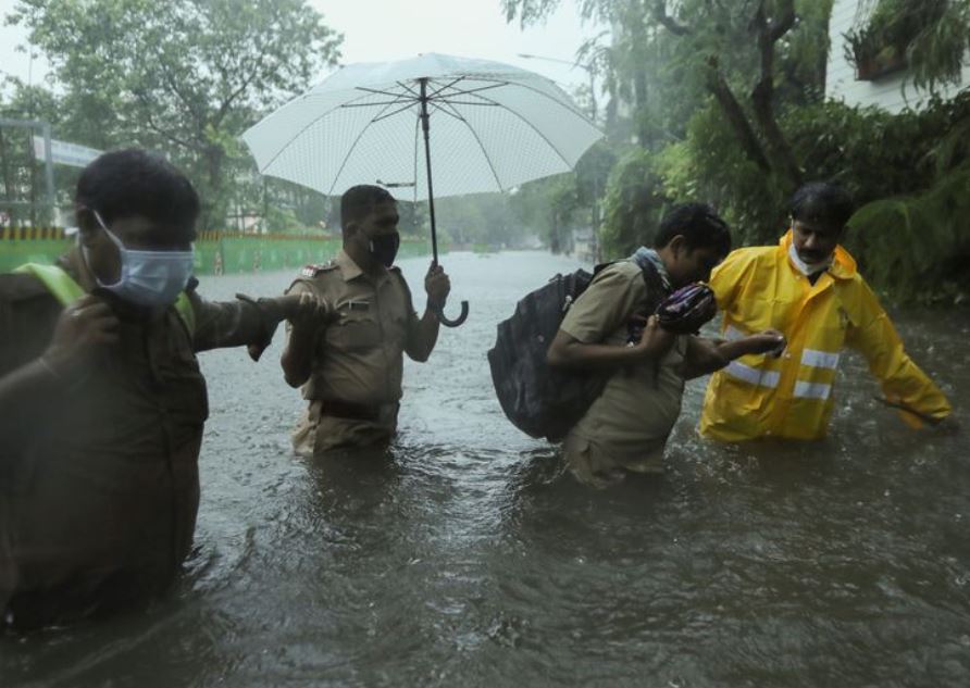 Frontline workers help people cross a flooded street after heavy rainfall caused by Cyclone Tauktae