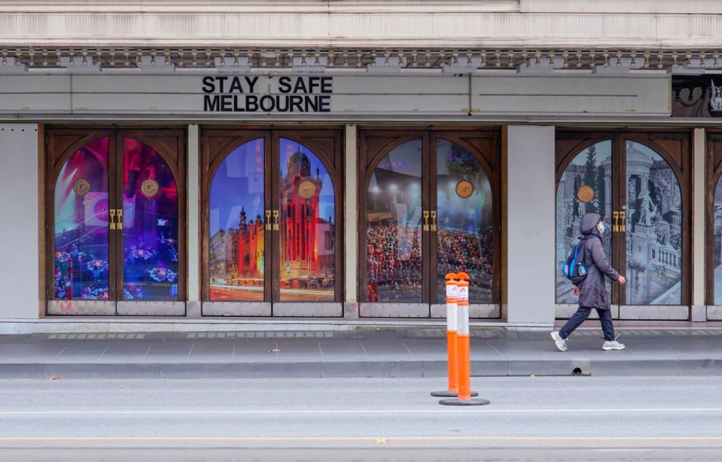 A woman walks past a "Stay Safe Melbourne" sign on a mostly-empty city centre street on the first day of a seven-day lockdown as the state of Victoria